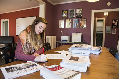 female student in a sweater and scarf at the rose oneill literary house, writing surrounded by event posters and publications