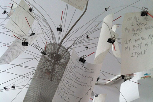 Poetry hand-written on pages suspended w/ binder clips on a display