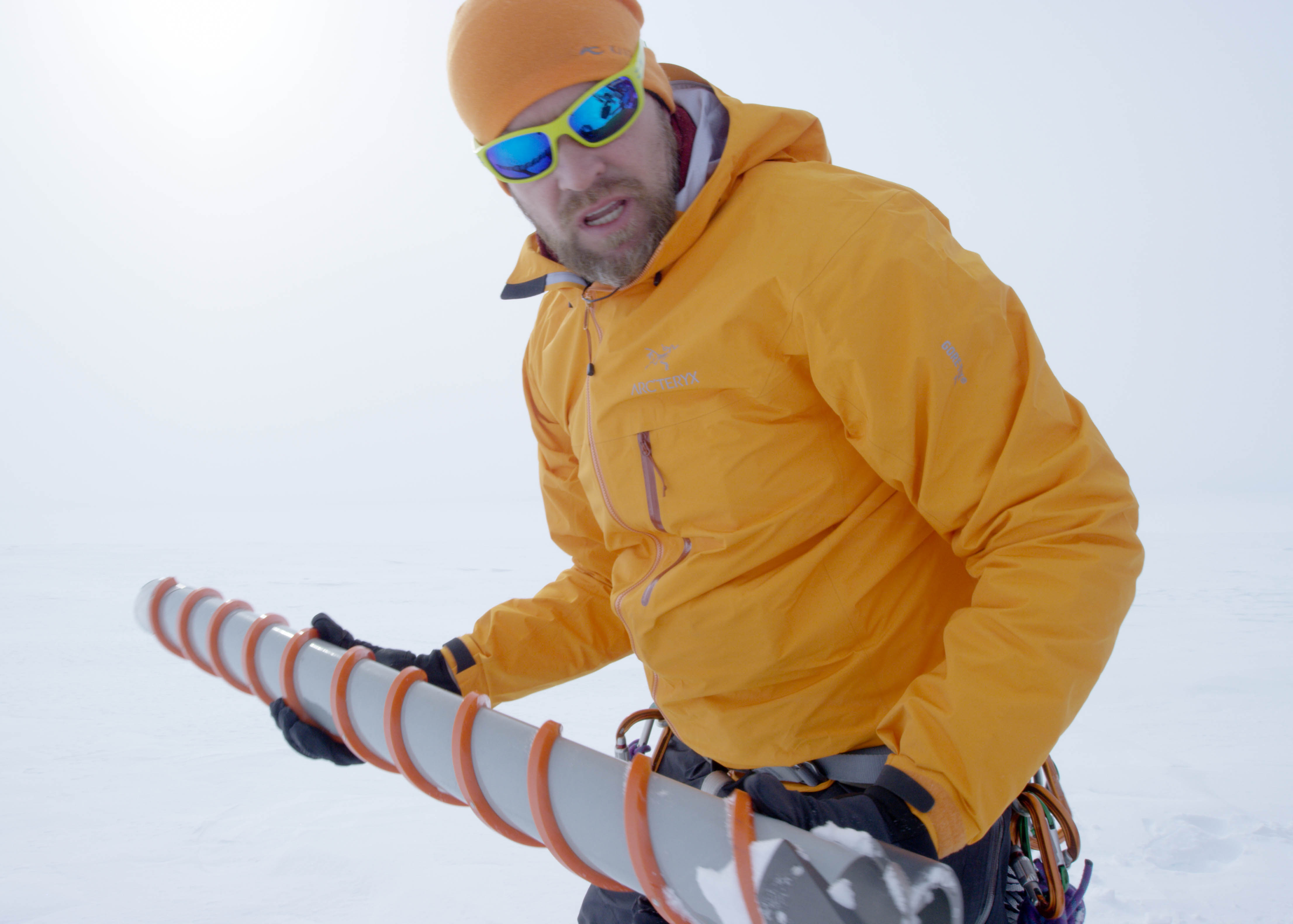 Glacier scientist Jason Box holds a study instrument in both hands while in cold weather gear in the snow