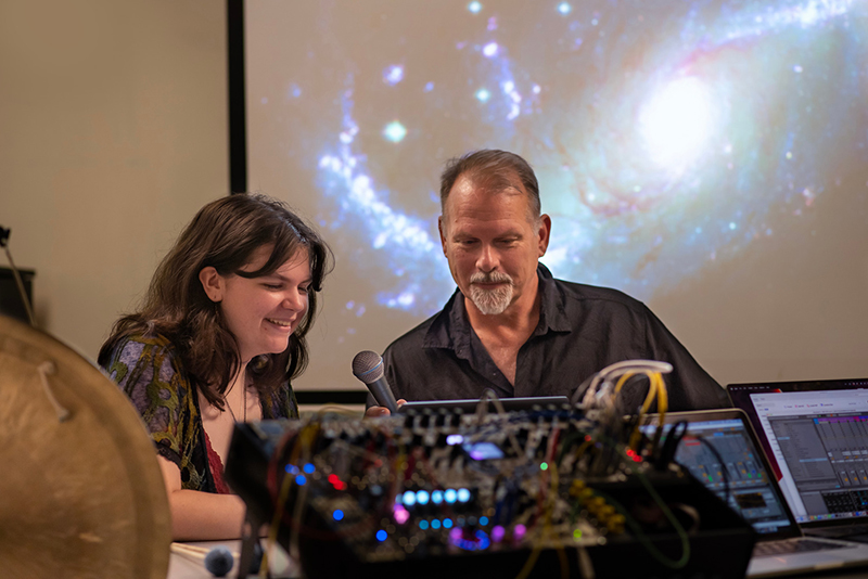 Stevie Lyles '26 and music professor Ken Scweitzer work with recording equipment in front of a projection of an image from the James Webb Space Telescope