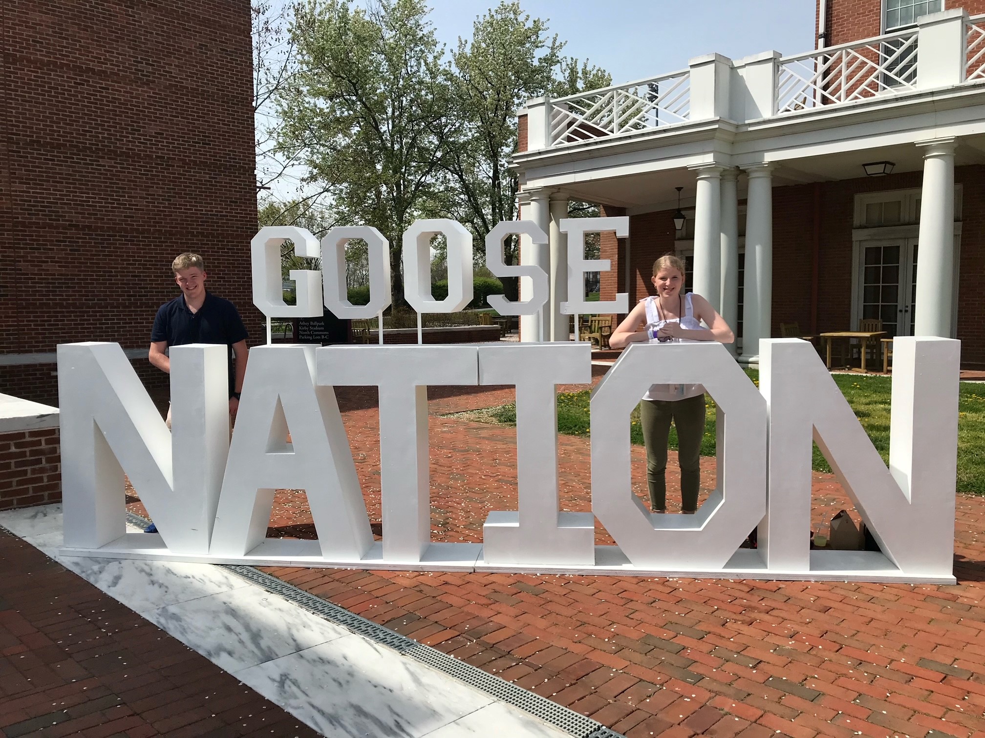 Osucha twins Kaitlin and Zach stand in Martha Washington Square behind large white "Goose Nation" sign.