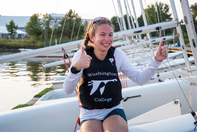 girl in WC life vest sitting on sailboat with two thumbs up