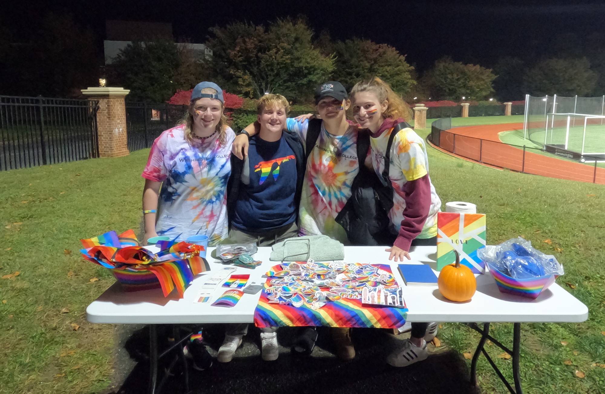 Four students offer rainbow materials to fans at a Washington College soccer game