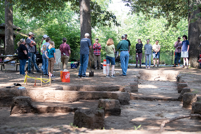 Volunteers listen to instructions from professor Julie Markin while standing by archaeological units excavated to varying depths.