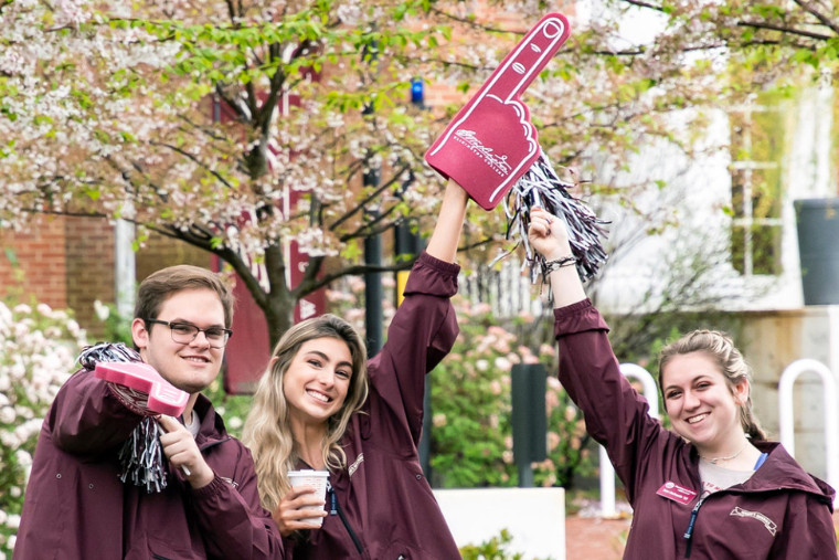 Three Washington College students smile with their arms in the air