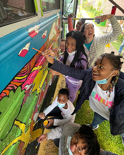 Students at Garnet Elementary School, a Title I school in Chestertown, help to paint the literacy mural on its sides as illustrator Robbi Behr looks on.