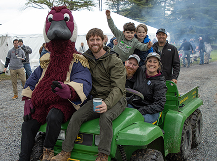 Gus the Goose, alumni, and families sit on a tractor at the annual Fish Fry event