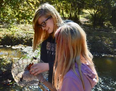 a Washington student showing a younger student what they caught in a dip net in a stream