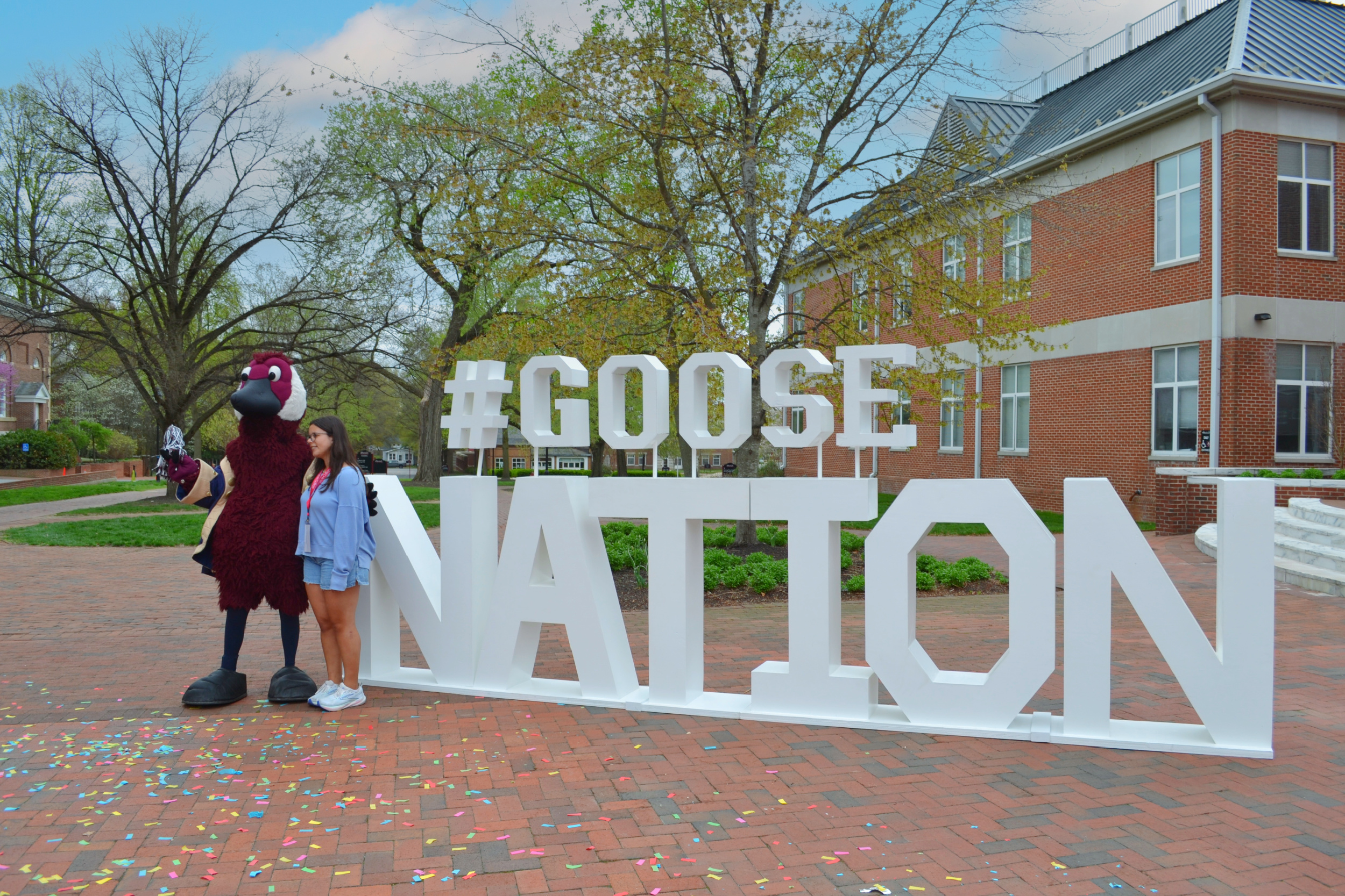 Washington College Student celebrating on Admitted Students Day with Gus in front of the Goose Nation sign.