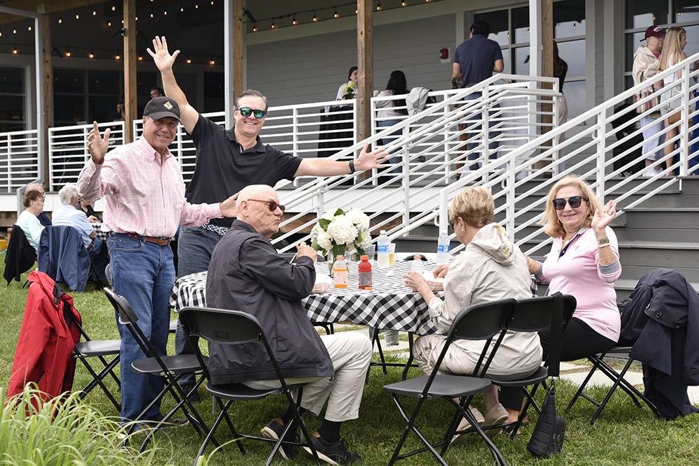 alumni wave from a table at an event at the boathouse