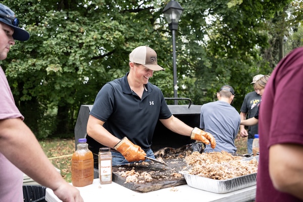 An alum prepares pulled pork at homecoming