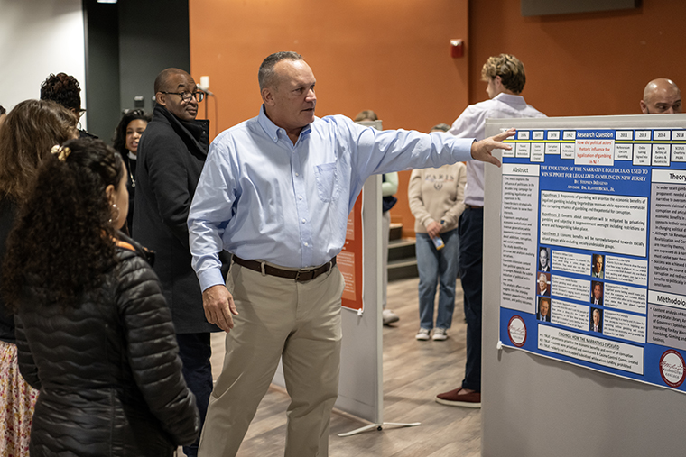 Steve DiEugenio '24 points to his poster during Senior Capstone Experience presentations for the political science department in December, 2023.