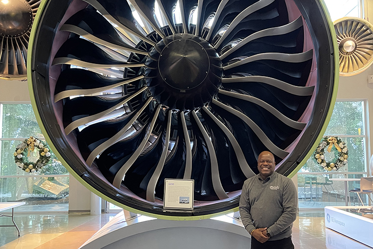 Vice President of Enrollment Management Johnnie Johnson stands in front of a jet engine at GE Aerospace before his presentation to employees there.