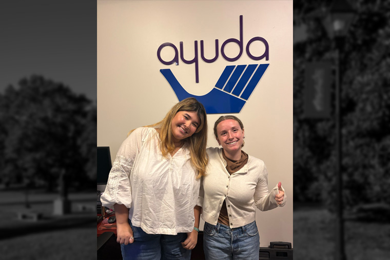 Eleanora Cardillo and Ana Arguello stand in front of the Ayuda sign