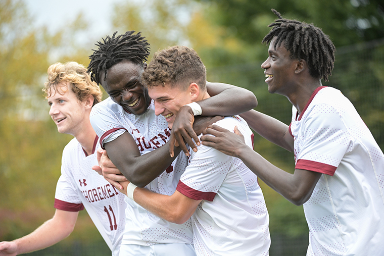 Four Washington College men's soccer players celebrate on the field.