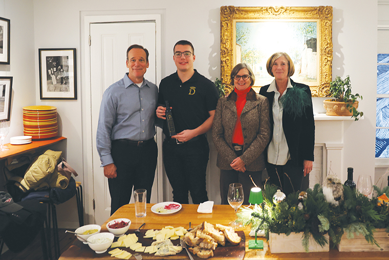 Holding a bottle of his olive oil, Bianti Danaj '24 stands with three guests behind a table set with bread and cheese.