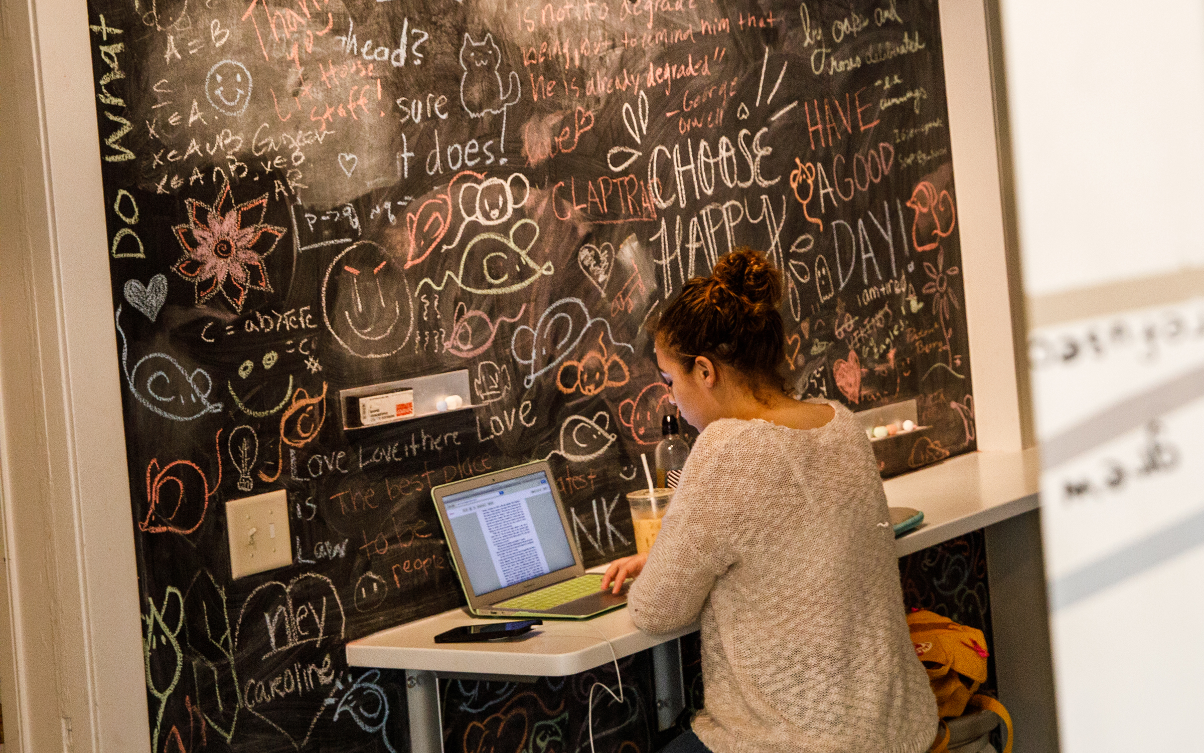 Student sitting in front of large chalkboard with phrases and doodles