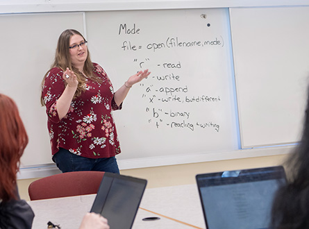 students and professor with code on whiteboard