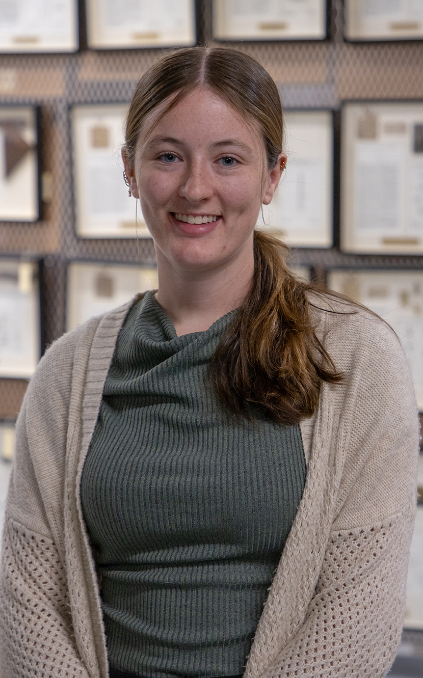 portrait of Cecilia Johnston ’27 stsanding in front of patent models in shadow boxes