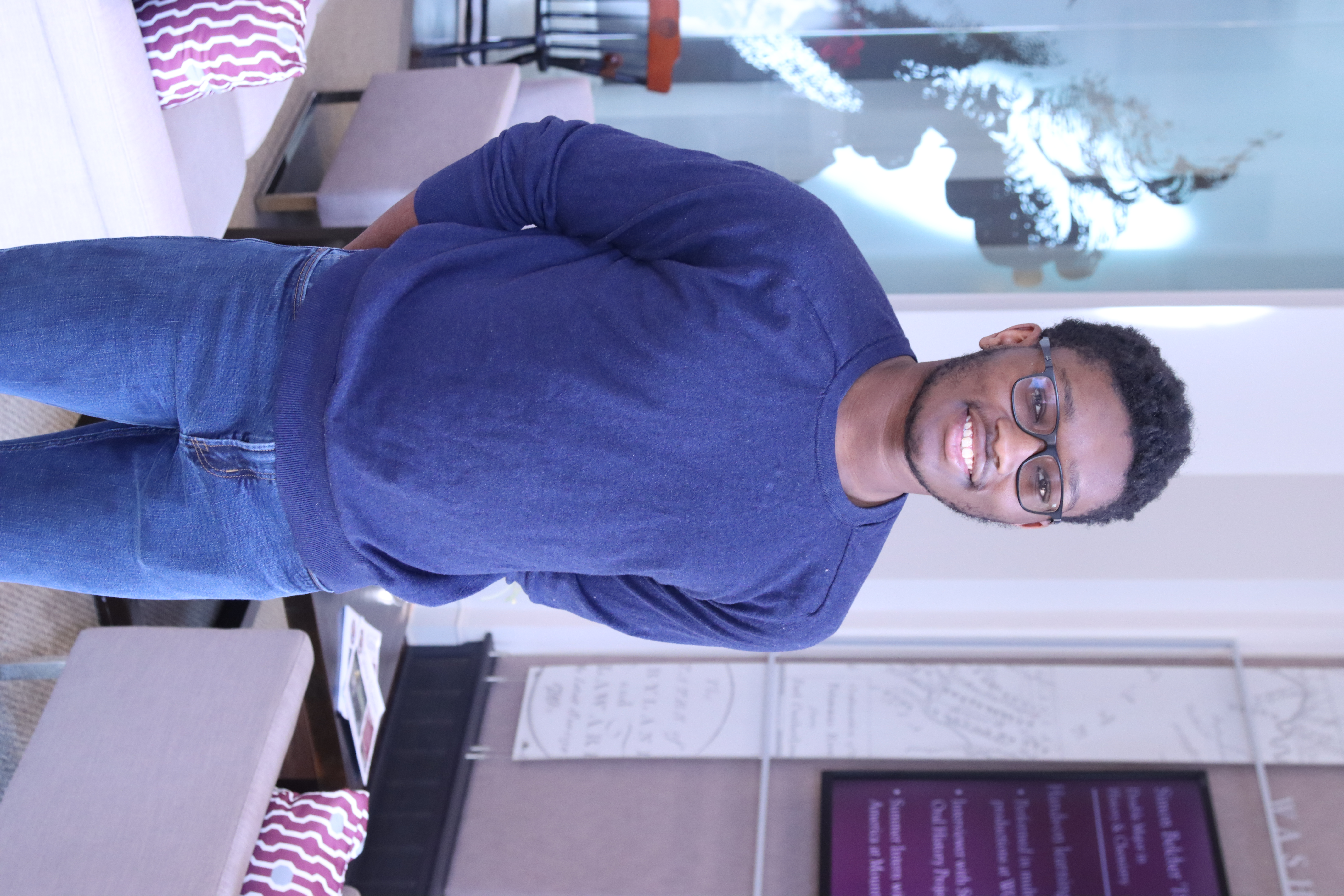 Jonah, smiling and wearing a blue shirt, jeans, and glasses. 