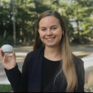 Sydney wearing a blue blazer, smiling and holding a brain with grass behind her. 